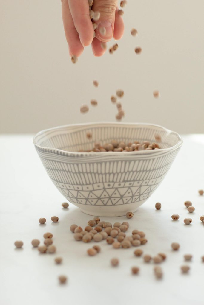 A hand pours mustard seeds into a patterned bowl, capturing the motion with elegance.